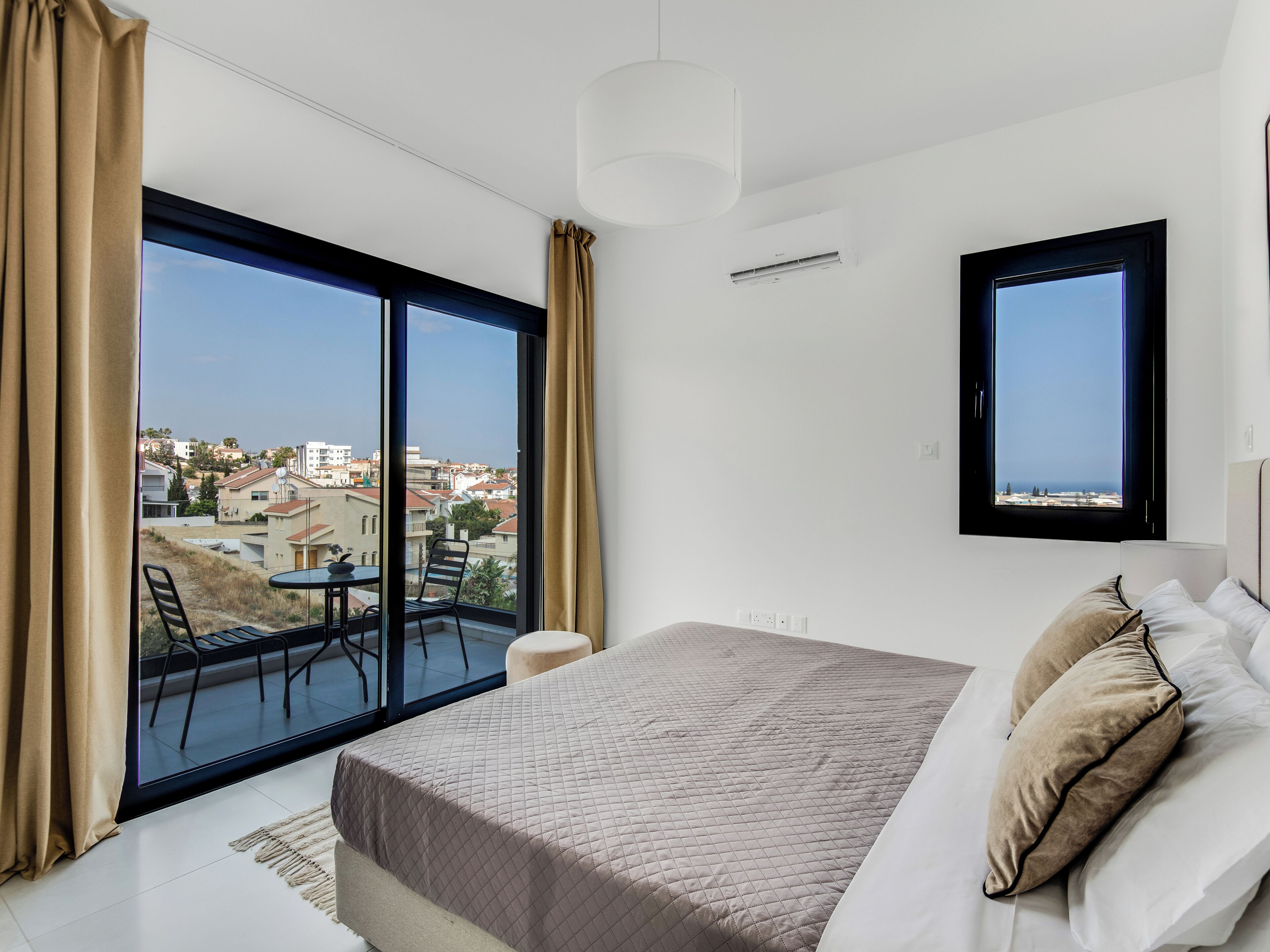A bedroom with a large bed, a view of the city, and a balcony with a table and chairs.
