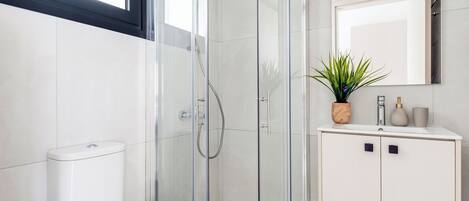 A modern bathroom with a glass shower enclosure, a toilet, a sink with a mirror, and a potted plant.