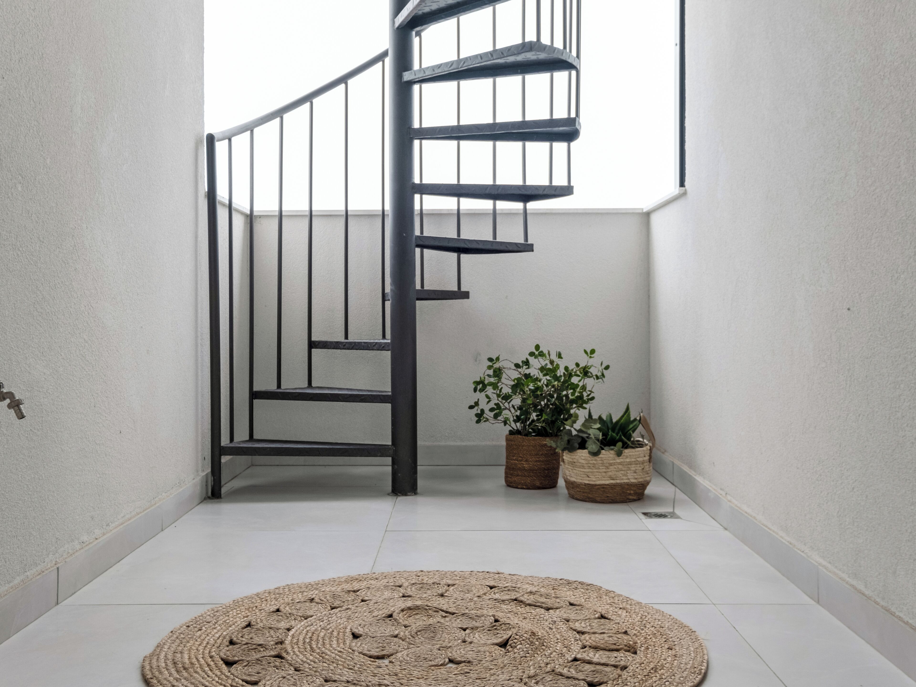 Eine Wendeltreppe mit Metallgeländern, ein gewebter Teppich auf dem Boden und zwei Blumentöpfe.