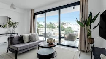 A modern living room with a grey sofa, a round black coffee table, and a large window with a view of houses and greenery.