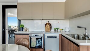 A modern kitchen with a dishwasher, oven, and sink. There is a wooden cutting board and a potted plant on the counter. - Sanders Elgio Limassol - Full Building (Limassol)
