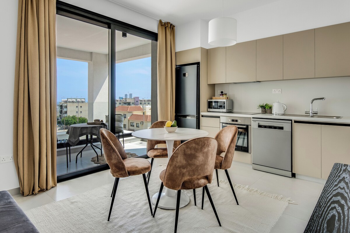 A modern kitchen with a dining area, large windows, and a view of the city.