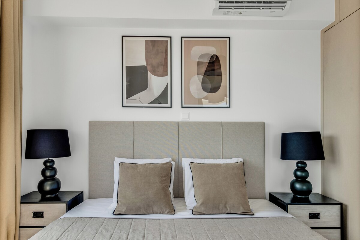 A modern hotel room with a large bed, two bedside tables, two lamps, and abstract artwork on the wall.