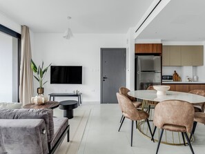Ein modernes Wohnzimmer mit einer Couch, einem Esstisch mit Stühlen, einem Fernseher und einer Küchenzeile mit Schränken und Geräten.