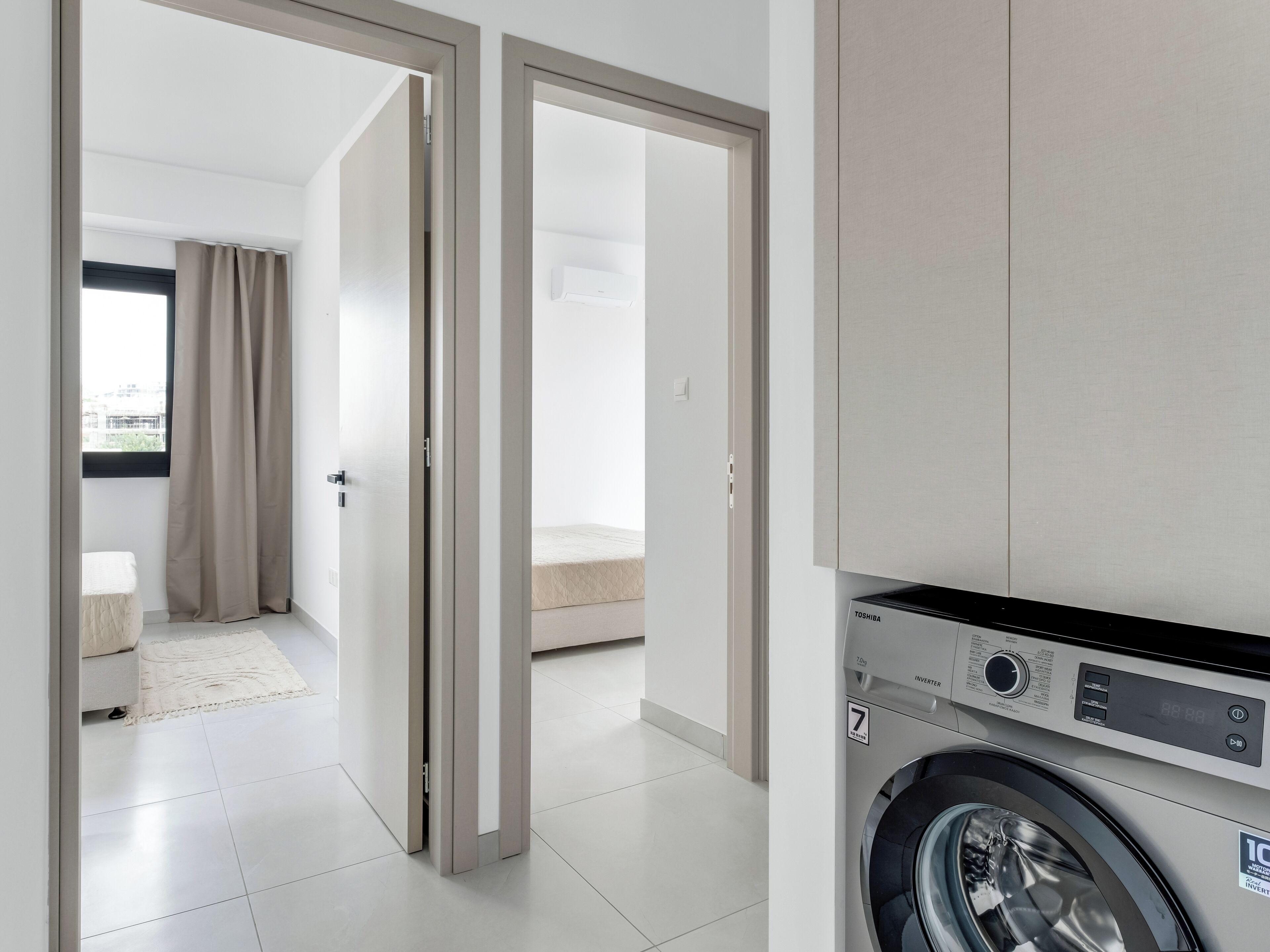 A modern apartment with a washing machine, a bed, and a bathroom visible through an open door.