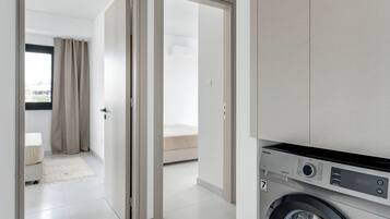 A modern apartment with a washing machine, a bed, and a bathroom visible through an open door.