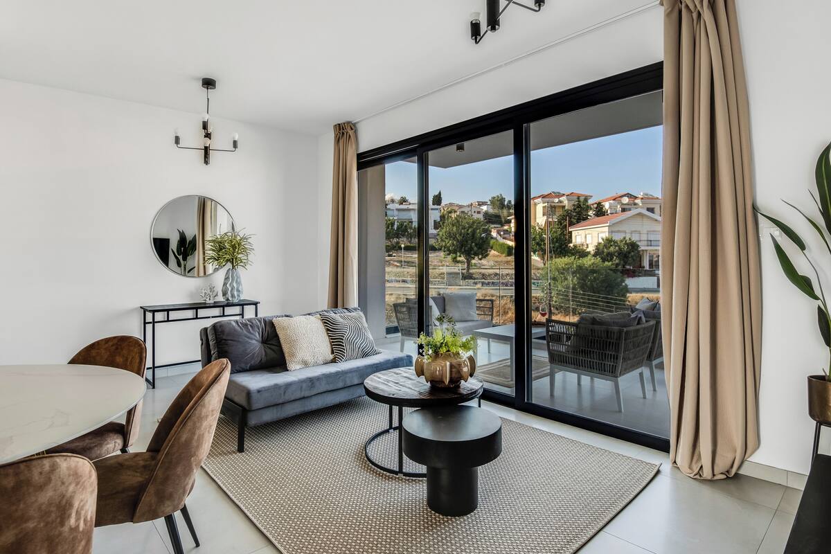 Un salon moderne comprenant un canapé, une table basse et un coin repas, de grandes portes-fenêtres coulissantes donnant sur un balcon avec vue sur la ville.