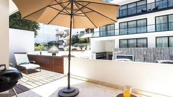 Una terraza en la azotea con una parrilla, sillas de descanso y una mesa con bebidas.