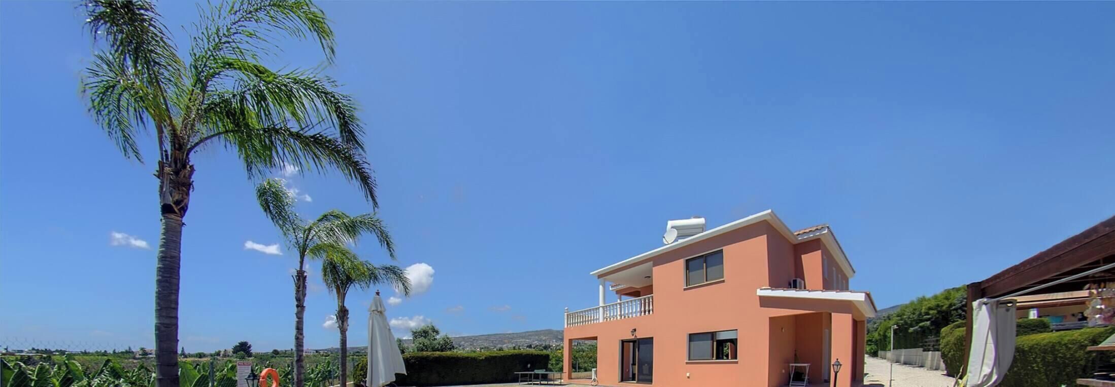 Una casa de dos pisos con balcón, rodeada de palmeras y un cielo despejado.