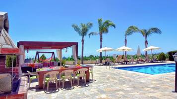 A poolside area with a barbecue setup, lounge chairs, and a clear view of the ocean.
