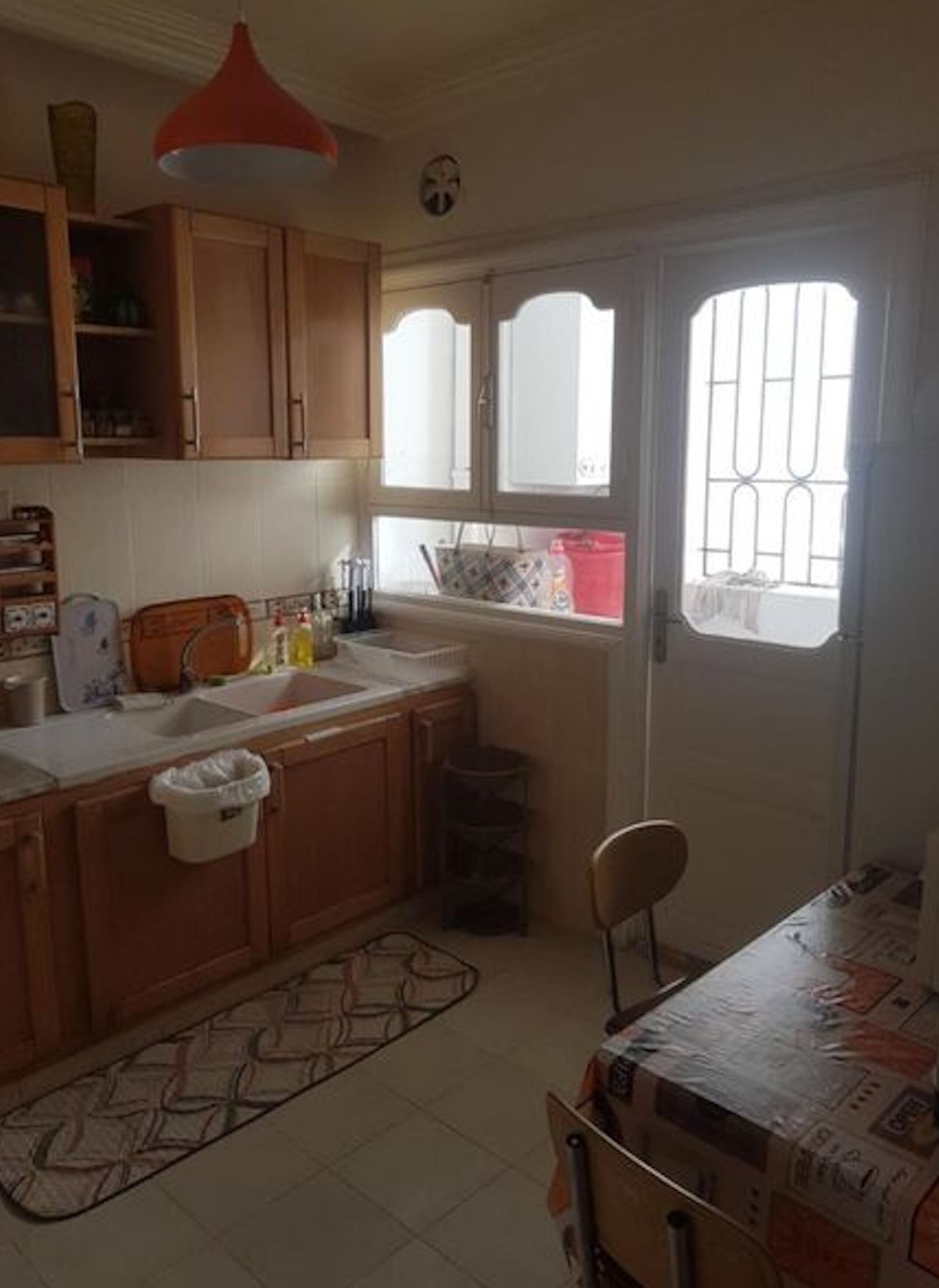 A kitchen with wooden cabinets, a sink, a window with bars, and a table with chairs.