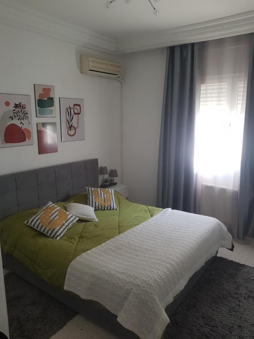 Un dormitorio con una cama doble, dos almohadas, una mesita de noche con lámpara y decoración en la pared.