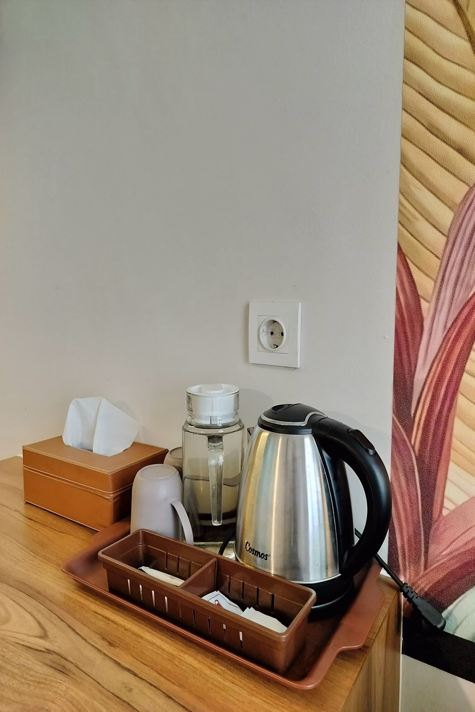 A wooden table with a tissue box, a glass water bottle, a stainless steel kettle, and a brown tray with compartments.