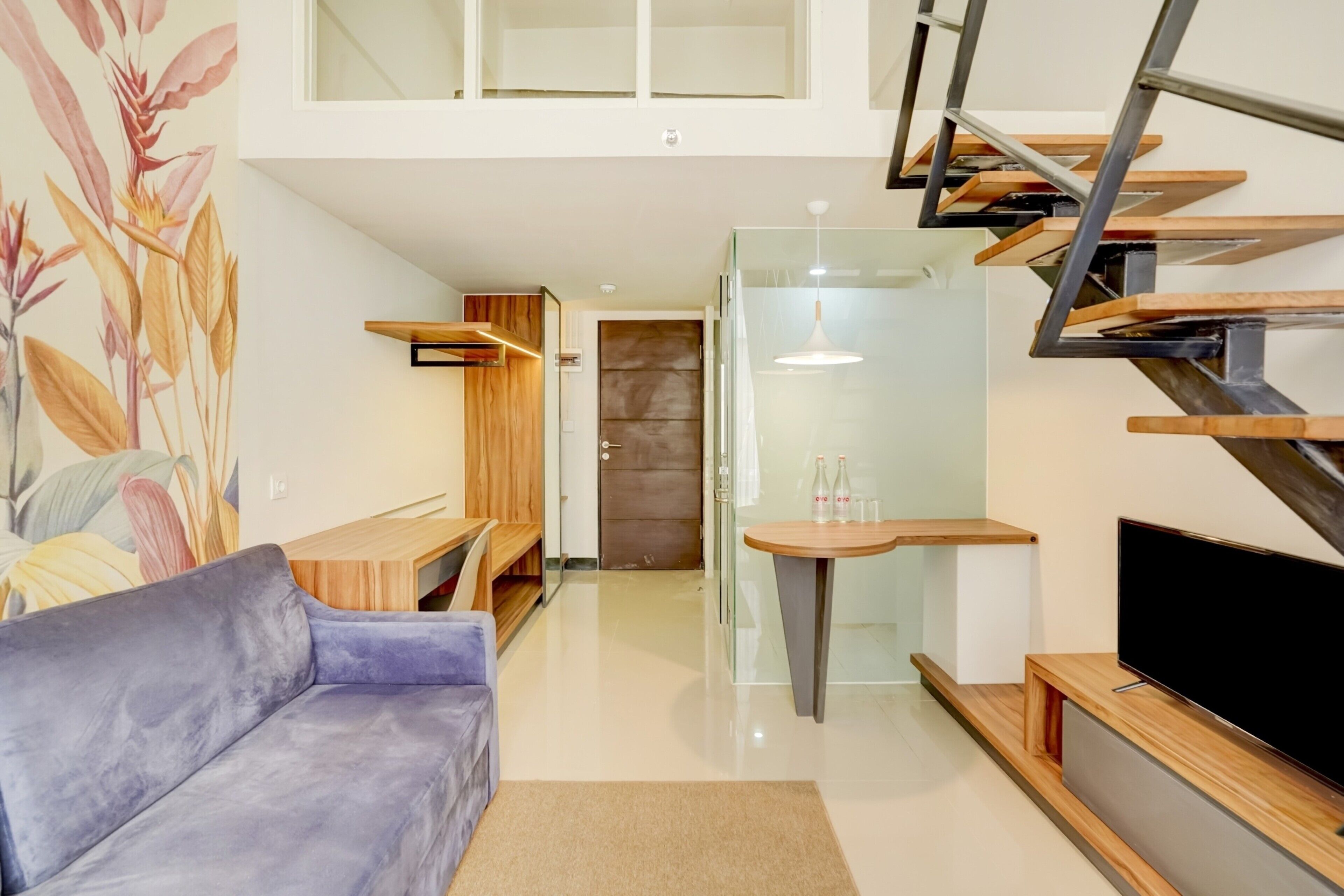 A modern living room with a sofa, a TV, a staircase, and a glass door leading to another room.