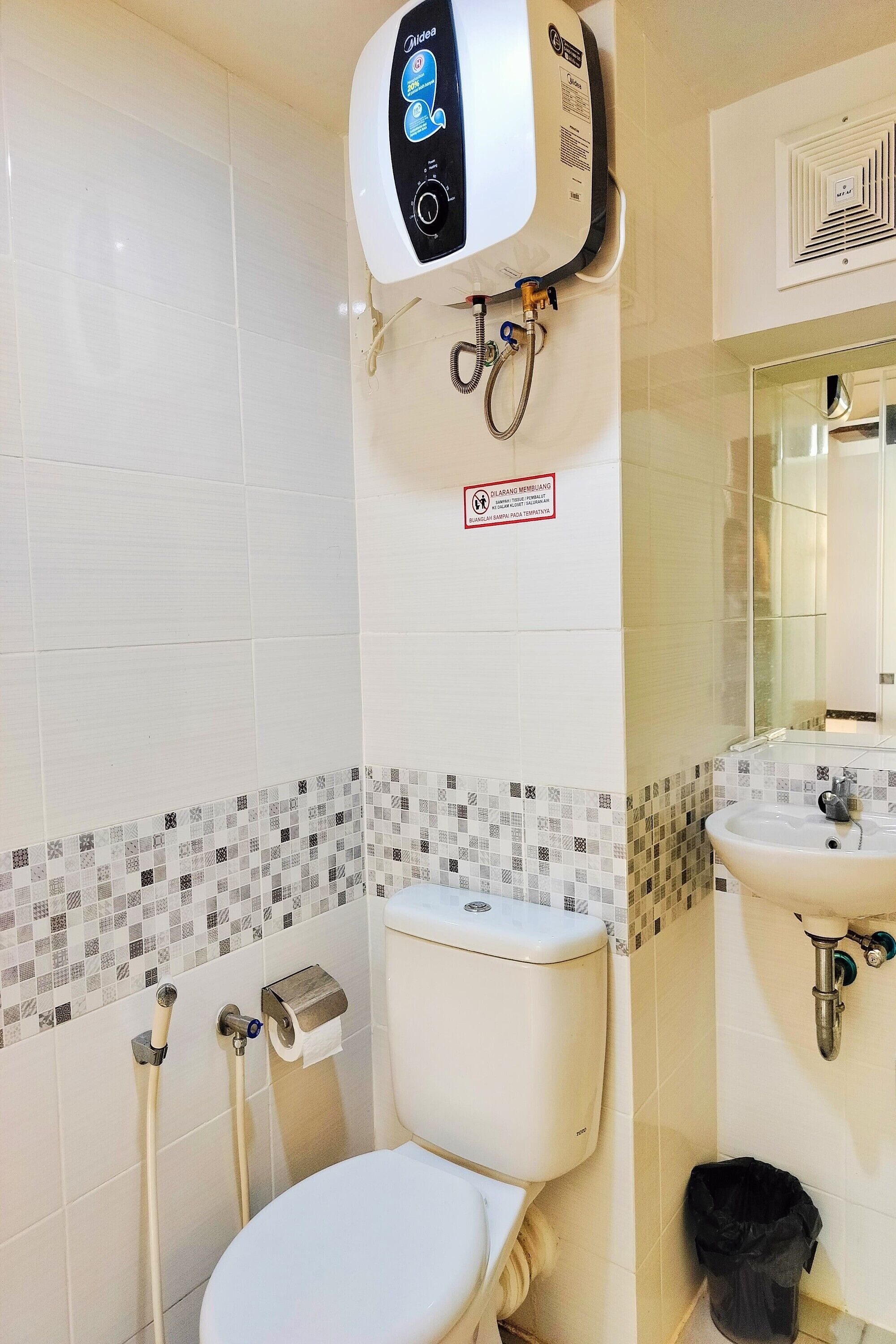 A bathroom with a toilet, bidet, and sink. There is a hand dryer mounted on the wall and a trash bin.