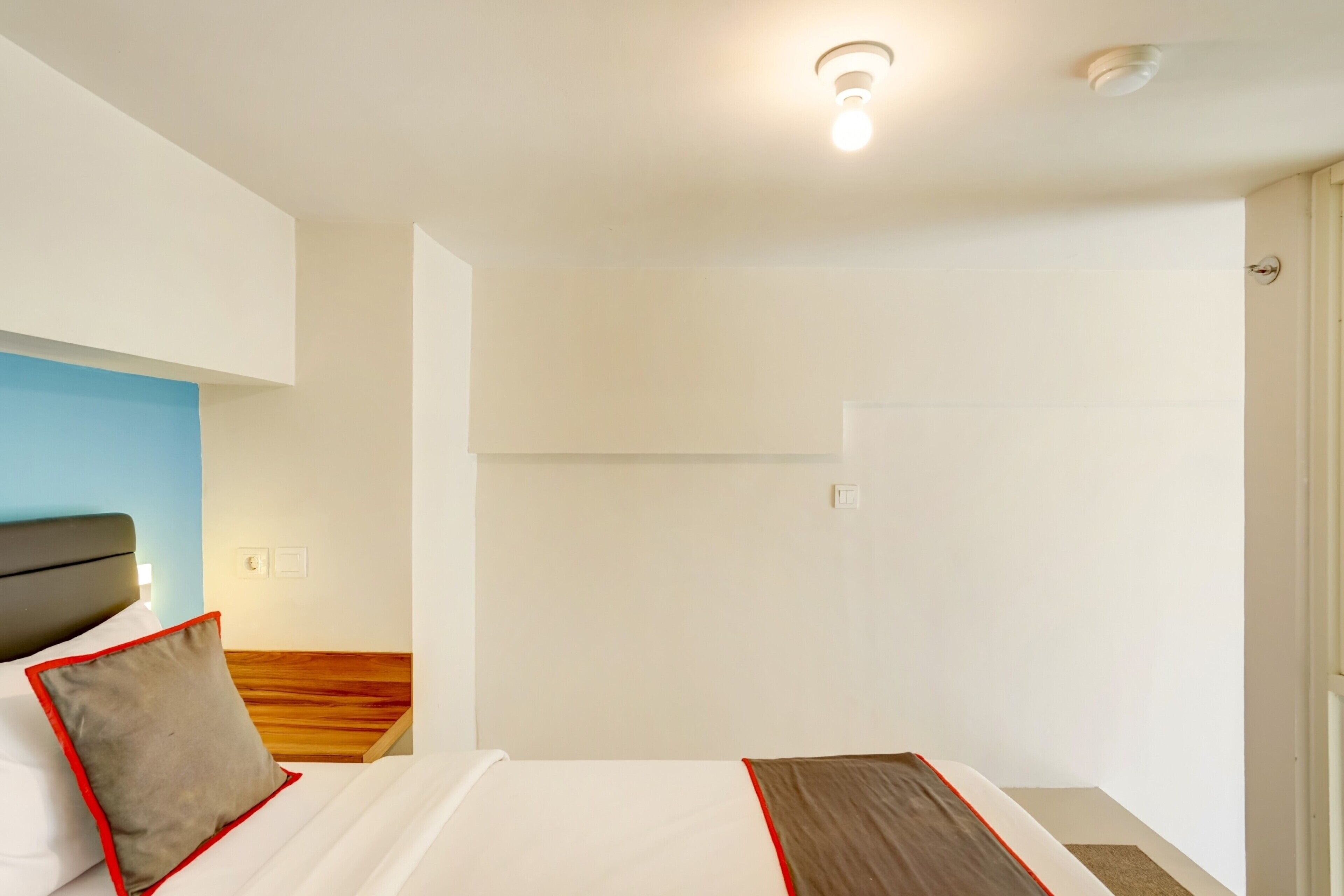 A hotel room with a bed, a wooden headboard, a white wall, and a door.