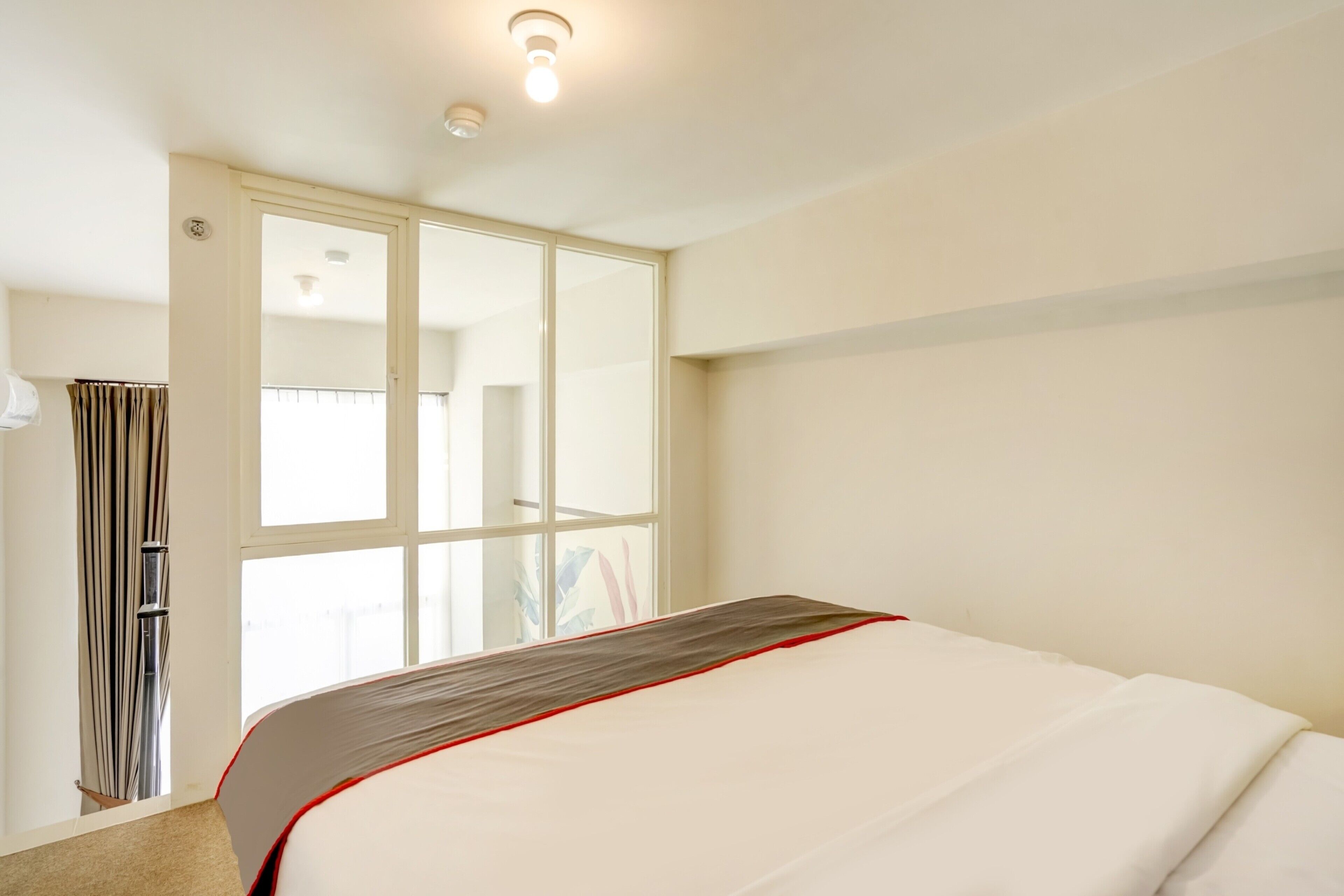 A hotel room with a bed, a window, a door, and a ceiling light.