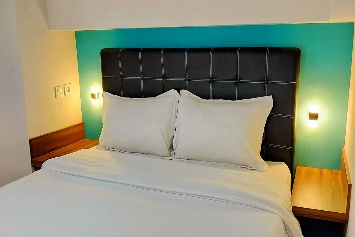 A neatly made bed with white linens and a black headboard, two bedside lamps, and a teal accent wall.