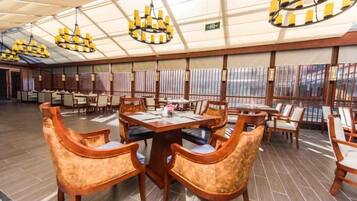 A spacious dining area with multiple tables and chairs, a high ceiling with chandeliers, and large windows.