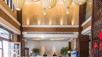 A hotel lobby with a reception desk, two staff members, and a large chandelier.