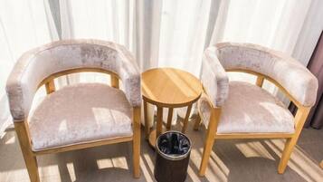 Dos sillones tapizados con estructura de madera y una pequeña mesa de madera, sobre un piso de baldosas, con un cesto de basura cerca.