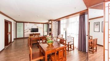 A spacious hotel room with a wooden dining table, chairs, a TV, and a large window with curtains.