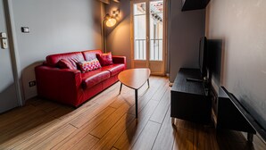 Een woonkamer met een rode bank, een klein houten bijzettafeltje en een zwarte entertainmentkast.
