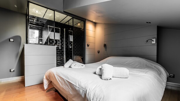 Een moderne slaapkamer met een groot bed, een inbouwkast en een douchecabine met glazen wanden.