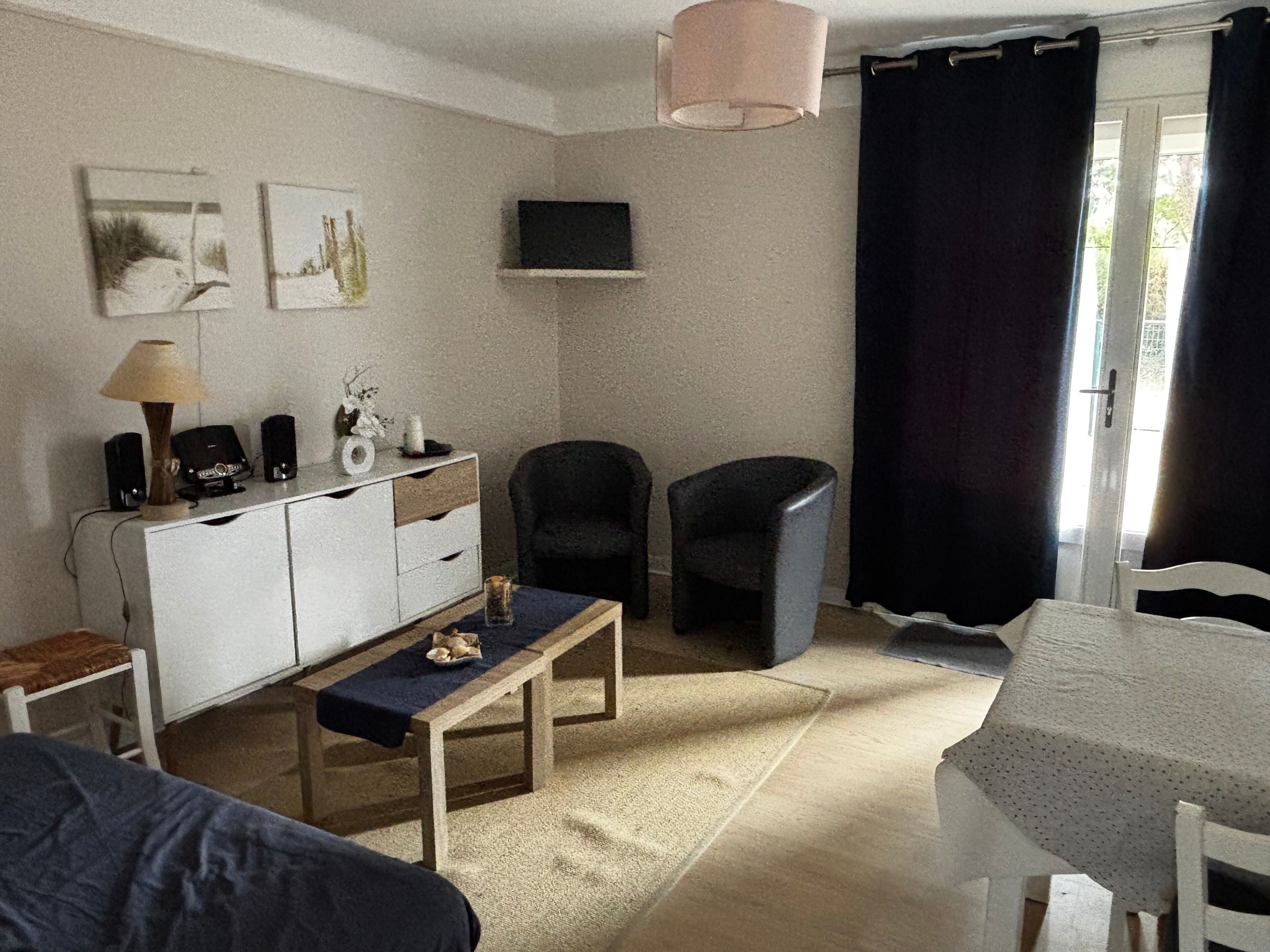 A room with a bed, a desk, a chair, a small table, a lamp, a television, and a window with curtains.