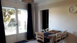 A dining area with a table and chairs, a clock on the wall, and a view through the door. - Ground Floor Apt with Garden 150m from Beach — Damgan / Pénerf (Damgan)