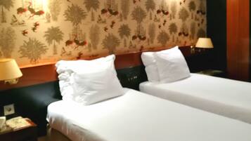A hotel room with two beds, a wooden headboard, a floral wallpaper, and two bedside lamps.