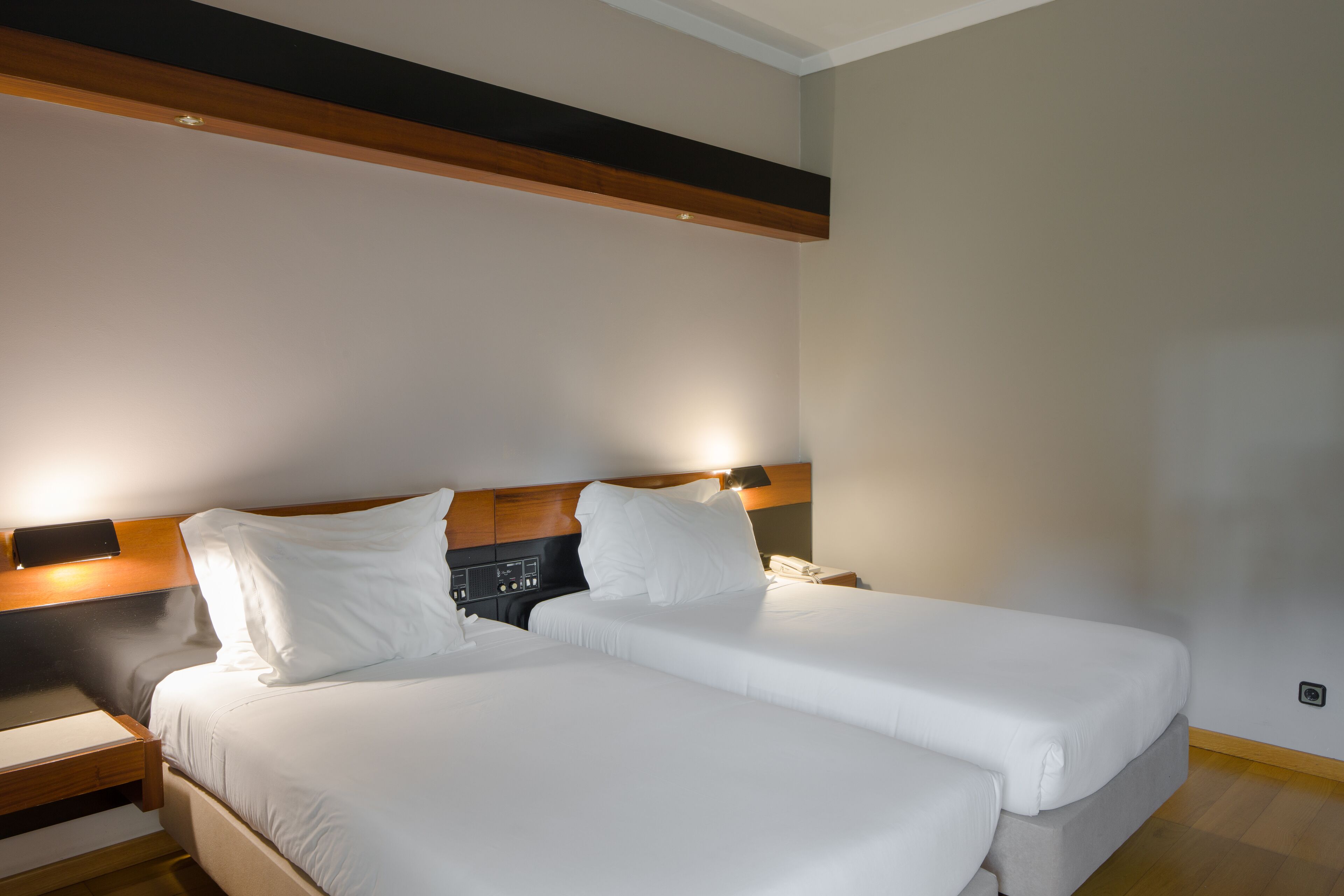 A double bed with white linens, a wooden headboard, a bedside table with a lamp, and a small nightstand.