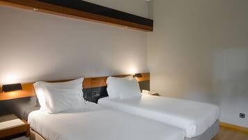 A double bed with white linens, a wooden headboard, a bedside table with a lamp, and a small nightstand.