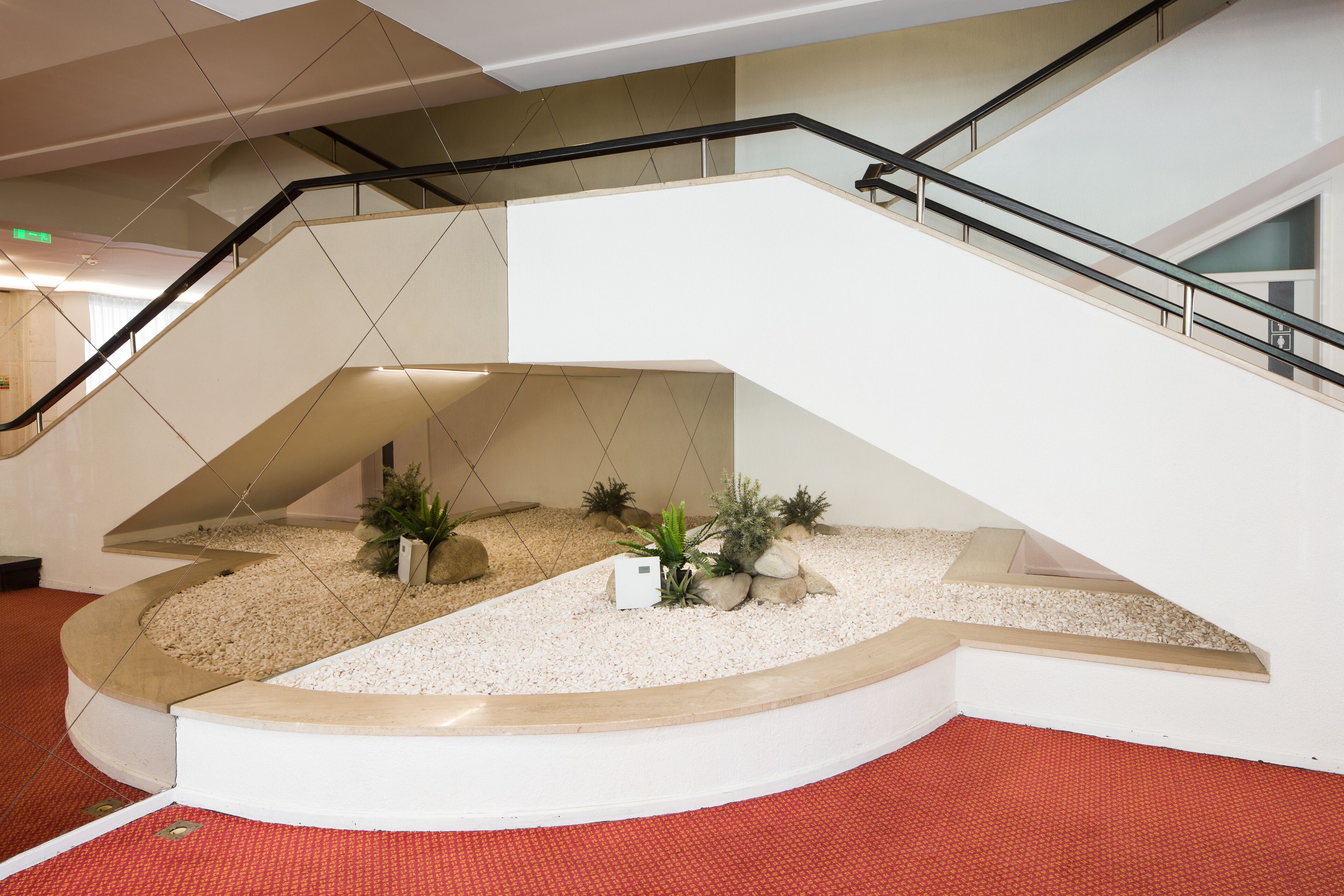 A modern interior with a curved staircase, a small indoor garden, and a red carpeted floor.