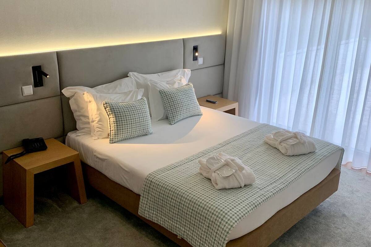 A modern hotel room with a large bed, a bedside table with a phone, and a nightstand.
