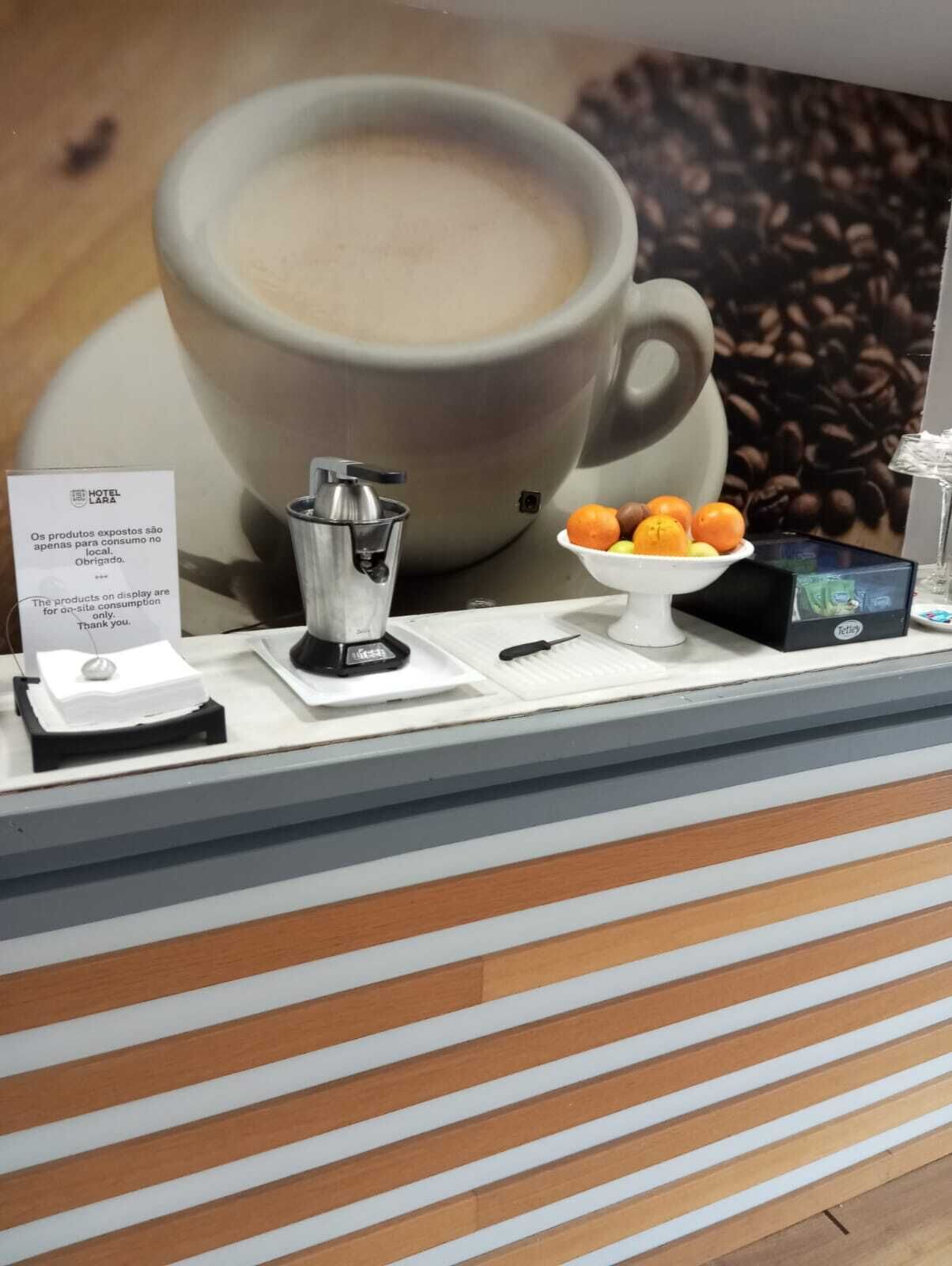 Un coin café équipé d’une machine à café, d’un panneau, d’un saladier rempli d’oranges et d’une boîte de café Tetra.