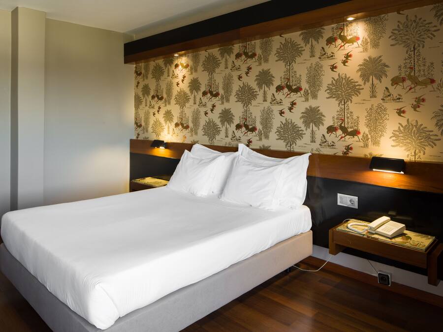 A large bed with white linens, a wooden headboard, and a nightstand with a telephone.