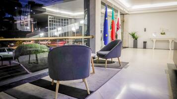 A modern lobby with two grey armchairs, a white table, and flags.