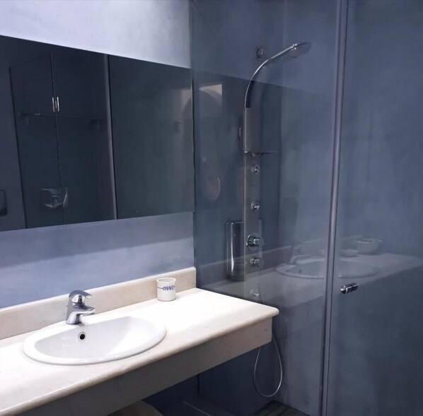 A modern bathroom with a glass-enclosed shower, a white sink, and a large mirror. - Maryo Village (Paros)