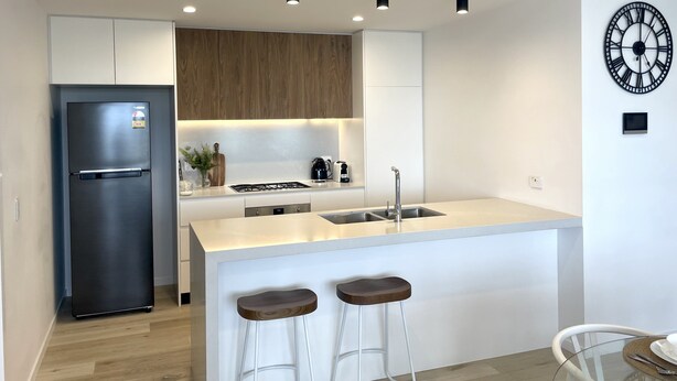 Una cocina moderna con refrigerador integrado, estufa y pileta. Hay dos taburetes de bar y una mesa de comedor con sillas.