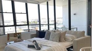 Un dormitorio moderno con una cama grande, un sofá y vistas de la ciudad a través de amplios ventanales.