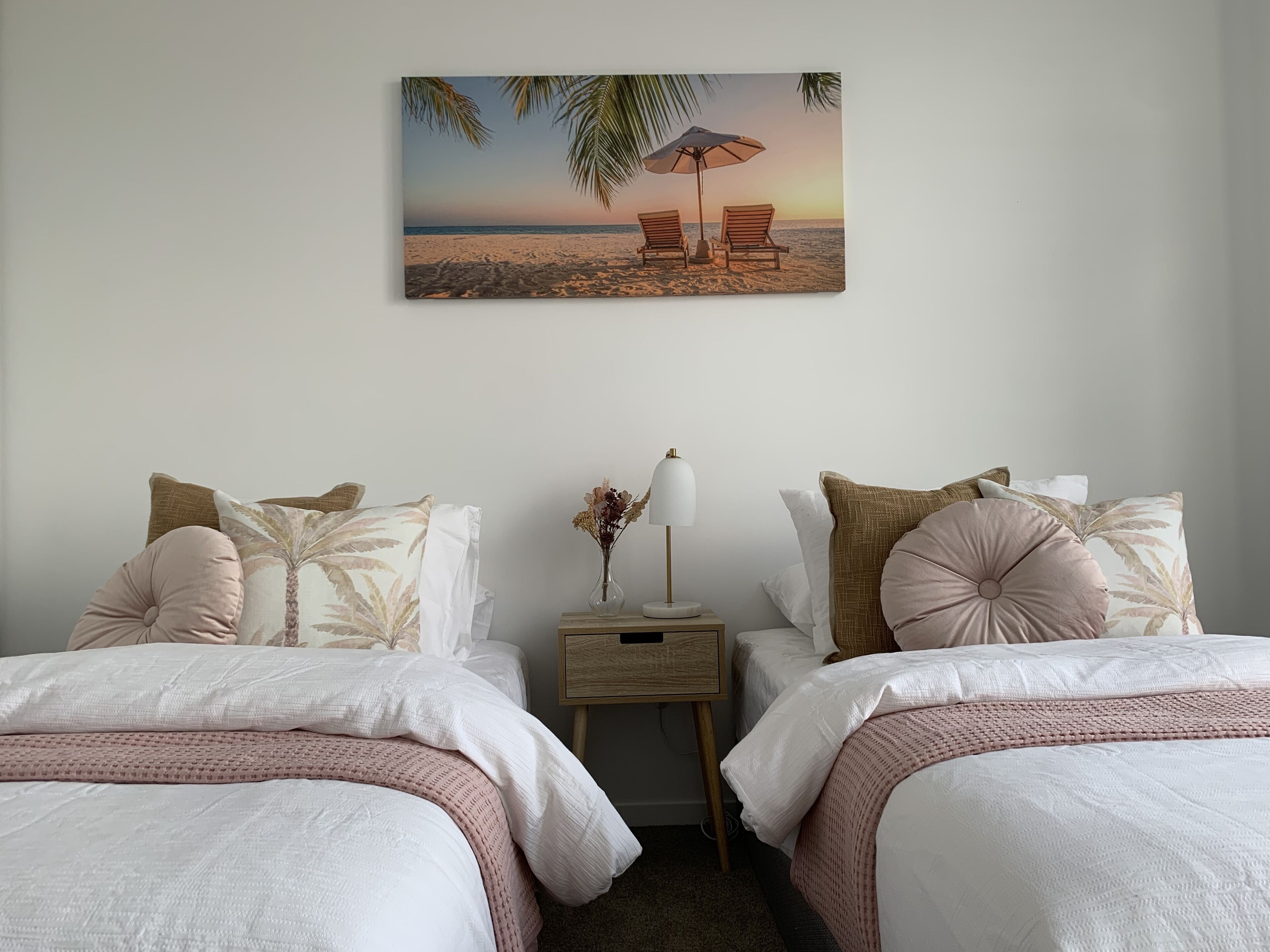 Ein Schlafzimmer mit zwei Betten, einem Nachttisch mit Lampe und einem Wandbild mit Meeresmotiv.