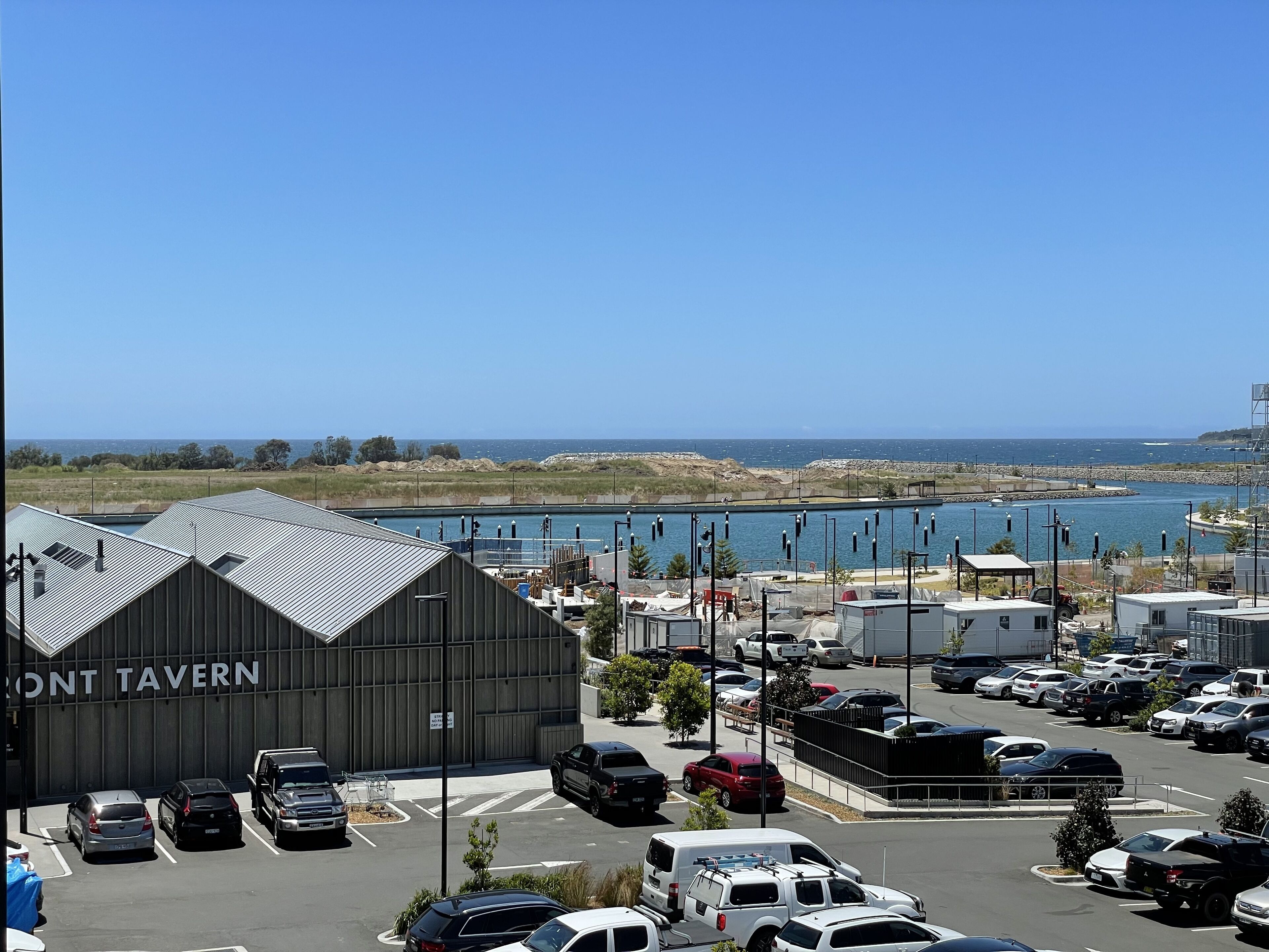 Un parking rempli de véhicules, un bâtiment portant l’inscription « MONT TAVERN », et une vue sur l’océan.