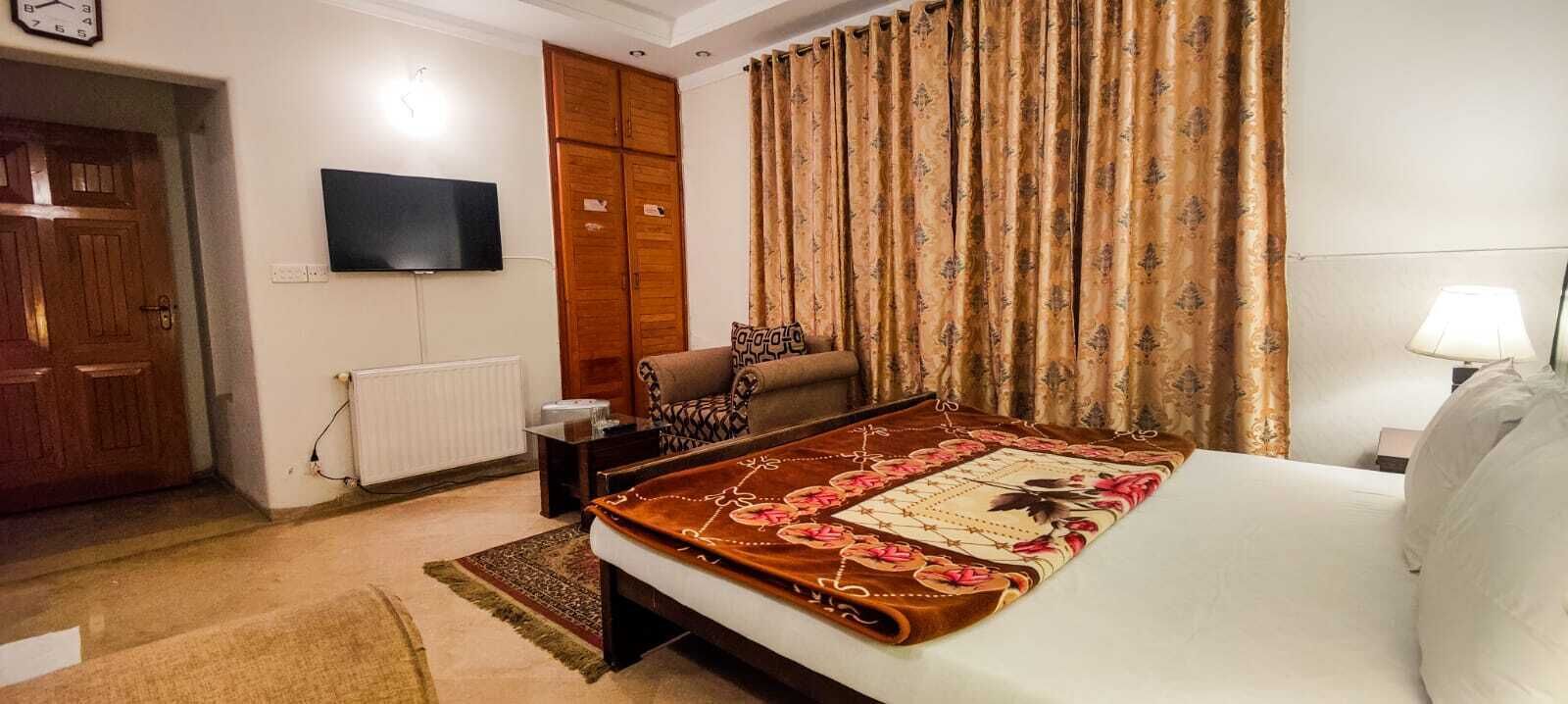 Ein Hotelzimmer mit Bett, einem an der Wand befestigten Fernseher, einem Kleiderschrank und Vorhängen.