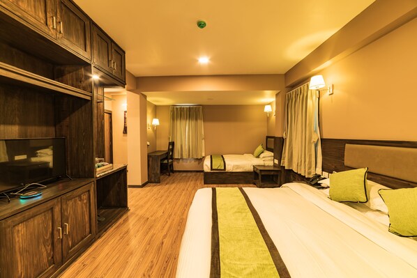 A hotel room with a large bed, a TV, a desk, and a chair. - Purnas Museum Resort (Jharuwarasi)