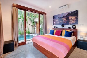 A bedroom with a large bed, a sliding glass door to a pool area, and a painting on the wall.