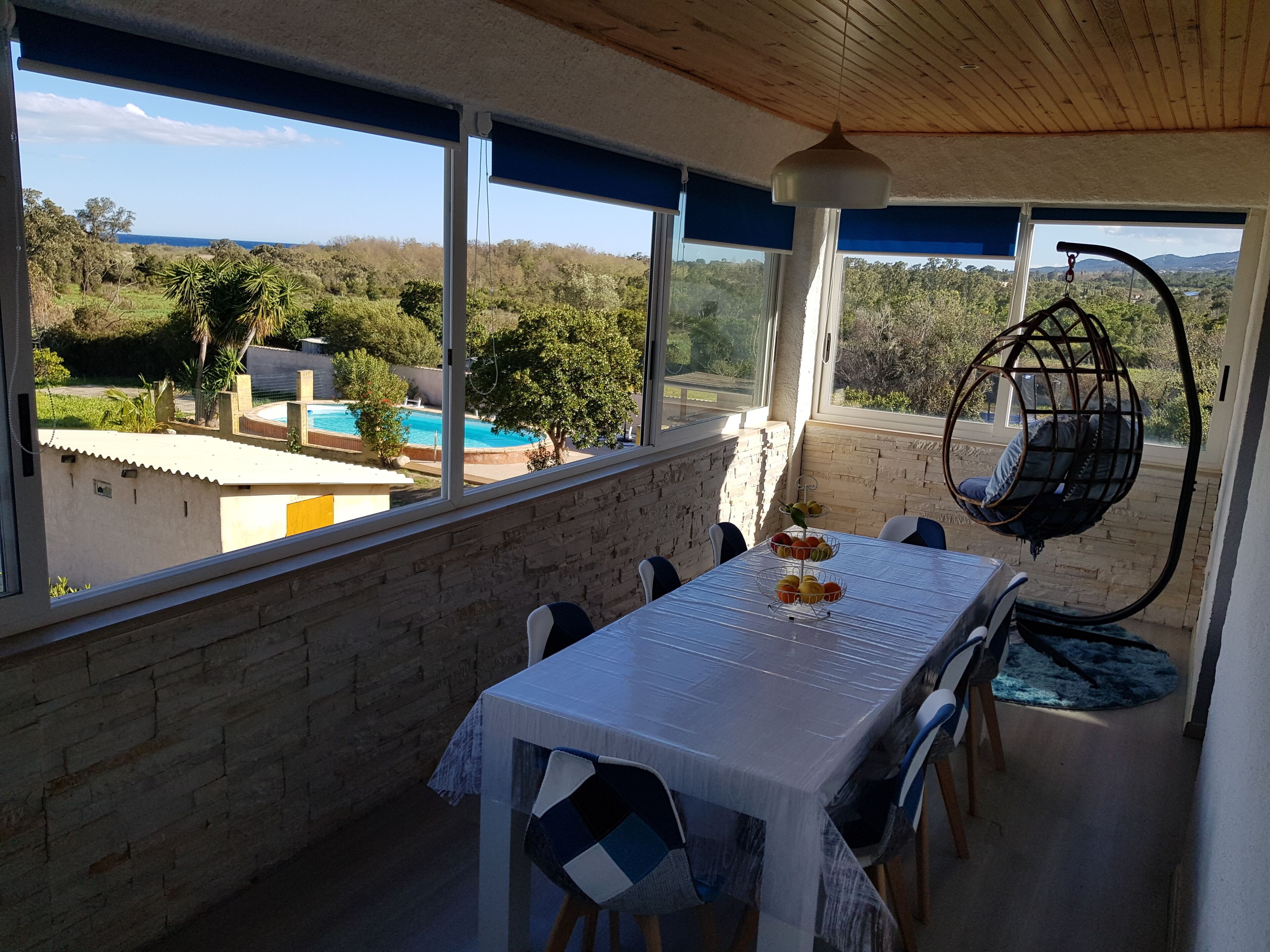 Ein Essbereich mit Tisch, Stühlen und einer Hängematte mit Blick auf einen Pool und viel Grün.