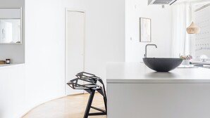 A modern kitchen with a large island, a hanging light fixture, and a wooden floor.