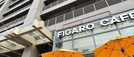 A modern building with the sign "FIGARO CAFE" and outdoor seating with yellow umbrellas.