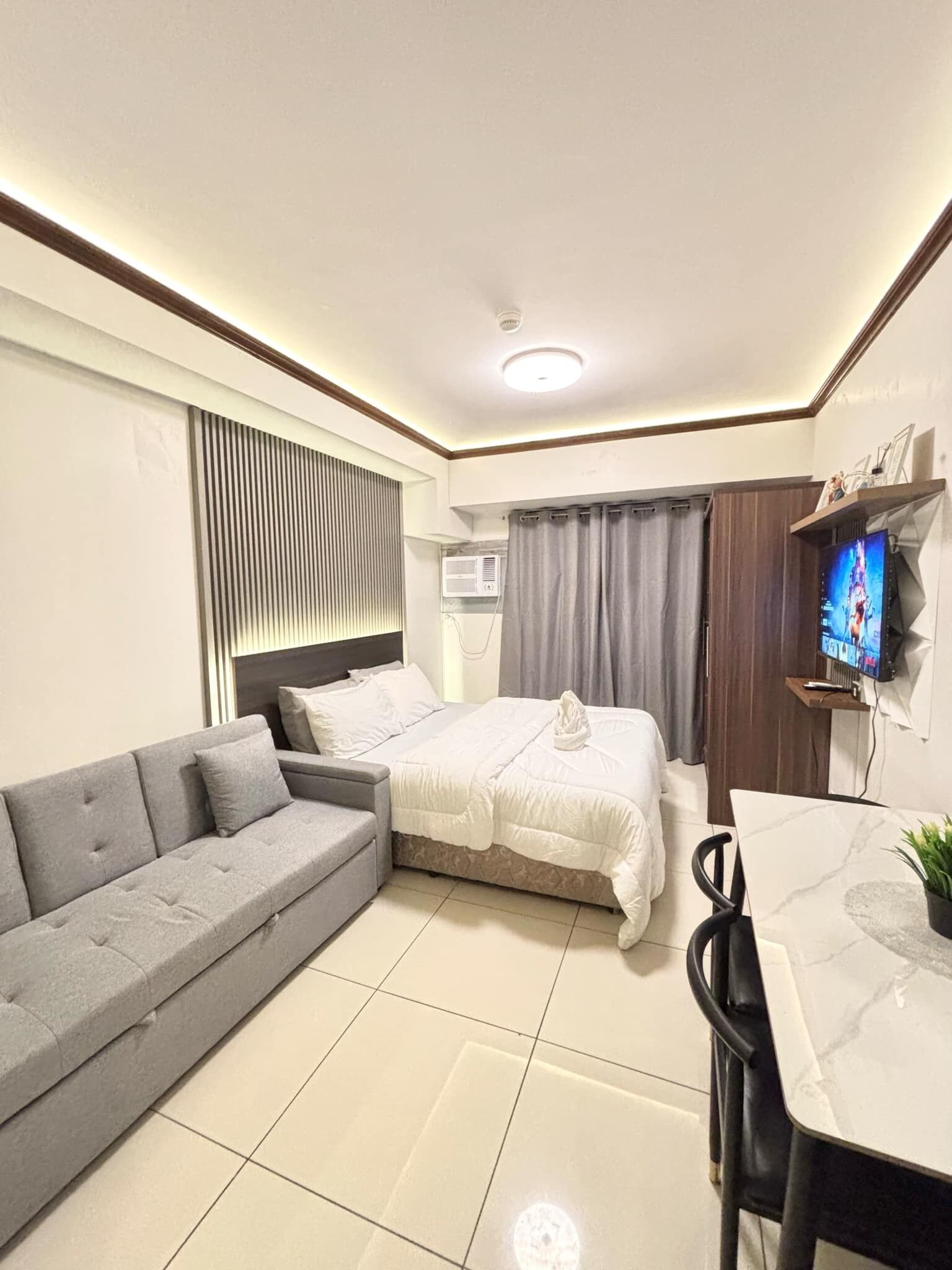 Een moderne hotelkamer met een bank, bed, televisie en een eethoek.